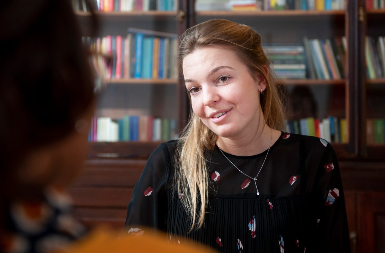 Eine jungen Frau im Gespräch mit einer Person, die nur im Anschnitt verschwommen zu sehen ist