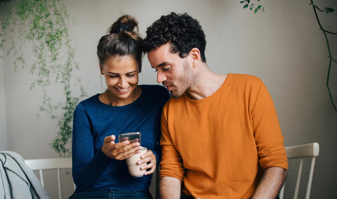 Junges Paar schaut interessiert gemeinsam auf ein Handy